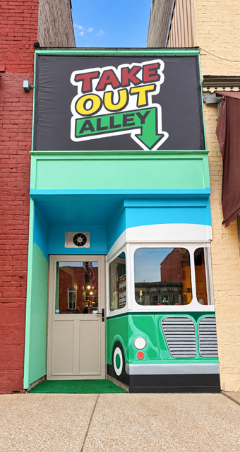 Take-Out Alley storefront with the restaurant sign and colorful bus design